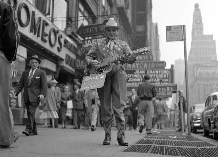A man playing a guitar promotes the film \"Johnny Guitar\" on the sidewalks of Times Square in the Spring of 1954.